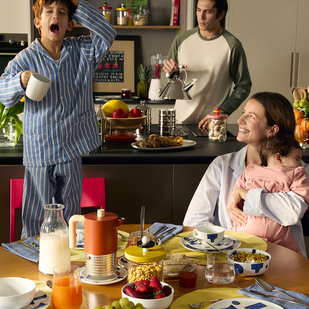 Family enjoys colorful breakfast in modern kitchen with Alessi products, warm and lively morning scene.